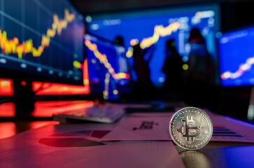 Silver bitcoin cryptocurrency token on desk in front financial analysis graph chart trading growth report on computer and laptop screen while broker meeting in shadow blurred background