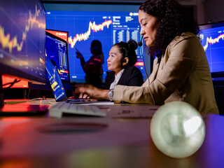 Female telesales marketing broker operators working buy sell trade cryptocurrency virtual money with customer online from laptop computer in office behind blurred silver bitcoin token in foreground