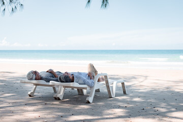 Retired couple resting on a adirondack chair by the beach in the sunlight and clean sandy beach. Retirement Planning Ideas and Happy Life.