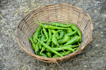 closeup the bunch ripe green chilly in the brown basket over out of focus brown background.