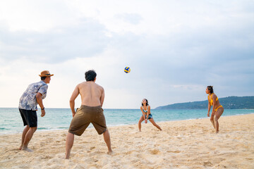 Fototapeta na wymiar Group of Asian man and woman friends playing beach volleyball together on tropical beach in sunny day. Male and female friendship enjoy and having fun outdoor lifestyle activity on summer vacation