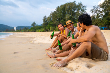 Fototapeta premium Group of Happy Asian man and woman friends sitting on the beach enjoy drinking beer with talking together at summer sunset. Male and female friendship relax and having fun outdoor lifestyle activity.
