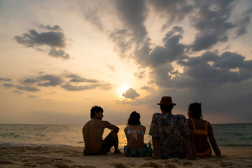 Group of Happy Asian man and woman friends sitting on the beach enjoy drinking beer with talking together at summer sunset. Male and female friendship relax and having fun outdoor lifestyle activity.