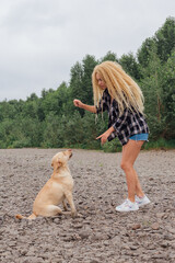 Young woman trains her labrador retriever dog on the river shore