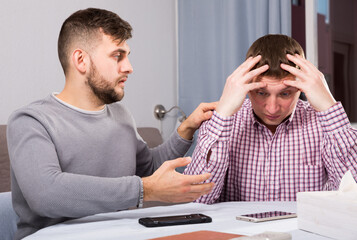 Fototapeta premium Man comforting his upset friend while discussing problems at table at home