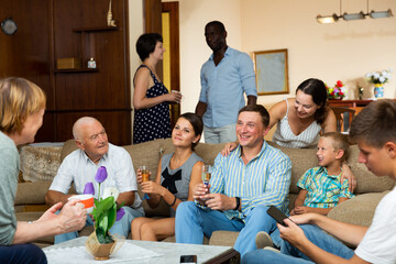 Big international family gathered together in parental home, cheerfully talking in living room