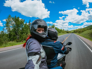 Motorcycle passenger young woman in a helmet makes selfie on action camera while riding on back of...
