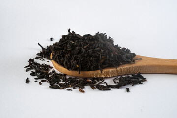 Bamboo wooden spoon full of black tea leaves, isolated on white, macro side view