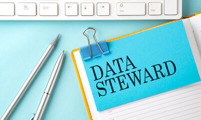 DATA STEWARD text on sticker on the blue background with pen and keyboard