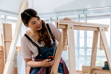 Portrait of young asian female carpenter assempling DIY wooden furniture with workshop background....