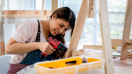 Portrait of young asian female carpenter assempling DIY wooden furniture with workshop background. Concept female worker