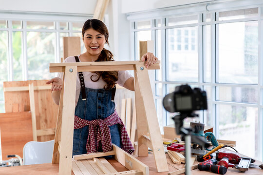 Young asian female carpenter showing and explaining DIY wooden furniture assembly to the camera. Recording video for online learning content.