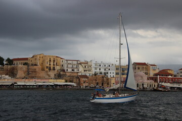 At the Sea, Rauer Tag an der See im Hafen Chania, Kreta, Griechenland, Wolken ziehen auf, im Vordergrund fährt ein Segelschiff