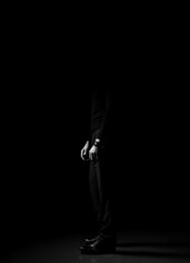 Black and white. Unrecognizable man in black trousers, sweater and shoes standing sideways over dark background. Lower body