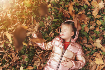 Little blonde girl plays with yellow autumn leaves in the garden, smile, has fun