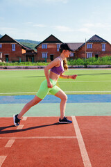 A sporty woman runs at the stadium. A girl trains on a treadmill. Sportswear. A bright sunny day and a blue sky.