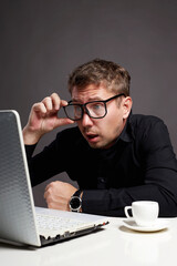 open-eyed Man sitting at a computer. funny boy in glasses