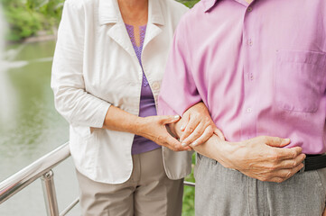 elderly couple, middle-aged man and woman, gently hold hands in summer nature. strong marriage for life. unrecognizable people. selective focus