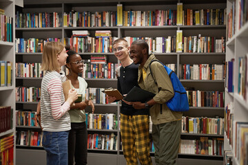 Waist up portrait of diverse group of students chatting while standing in school library, copy space