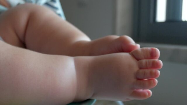Close up of bouncing baby moving barefoot feet with energy in baby cradle