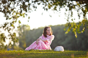 beautiful girl in a vintage rose dress walks by the lake with a white fluffy rabbit