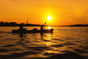 Silhouettes of people in boat at sunset. Man and woman ride boat on river. Small family trip
