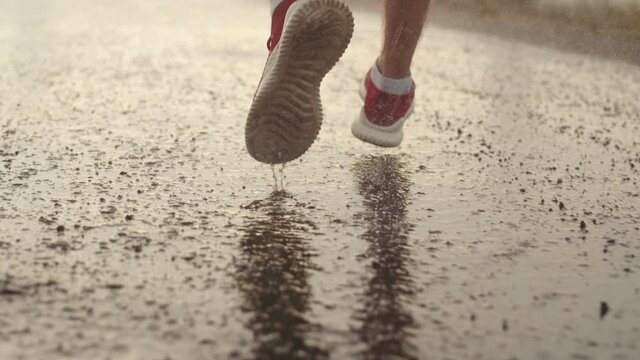 Legs of athlete in red sneakers stand during rain and start running, back view, closeup. Runner stands on road in rain and starts running