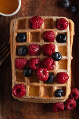 Fresh homemade Belgian waffles on an old wooden table with raspberries, blueberries and honey.