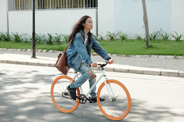 Fototapeta na wymiar Handsome young man with long hair riding on bicycle hurrying to college or work