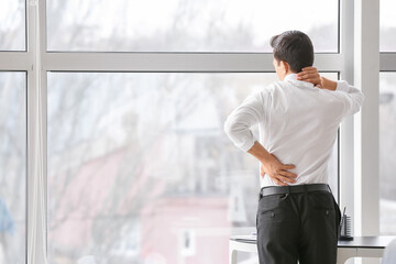 Fototapeta premium Young man suffering from back pain in office