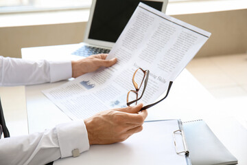 Young businessman with eyeglasses reading newspaper in office