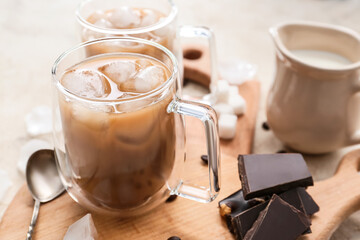 Wooden board with glass cup of tasty iced coffee and chocolate on table, closeup
