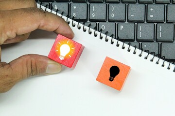laptop keyboard, white paper, hand holding light bulb and dim bulb left