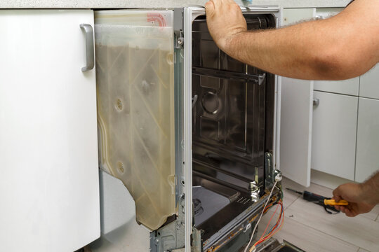fixing a home dishwasher. the master pulls out the built-in dishwasher for repair