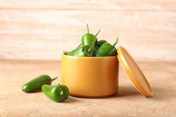 Bowl with green jalapeno peppers on color background