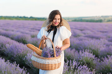 Beautiful young woman with basket for picnic in lavender field