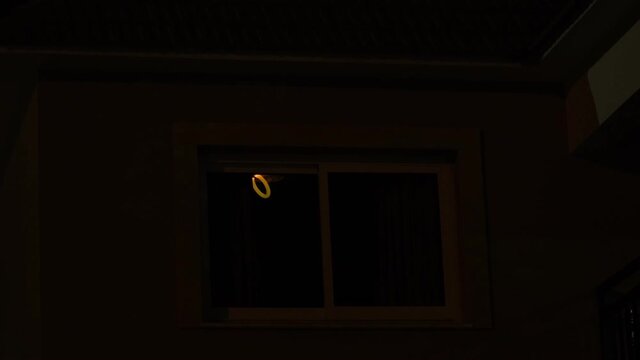 Light from the window of the house in the dark evening time. room lights up then turns off.