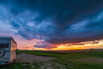 Sunset dramatic sky over camper van in Orcia Valley, Tuscany, Italy. Epic clouds above unique hill...