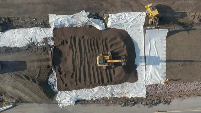 Excavator leveling soil while dump truck unloading gravel on road construction.