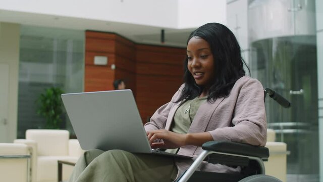 Afro-American businesswoman in wheelchair typing on laptop while working in office center