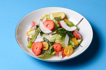 Spinach salad with strawberries, cherry tomatoes and coconut chip slices in a white plate over pastel blue background.