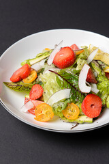 Spinach salad with strawberries, cherry tomatoes and coconut chip slices in a white plate over black background.