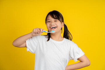 Little girl holding a tooth brush on a yellow background.