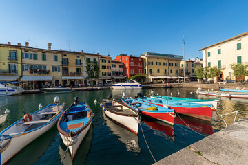 Fototapeta na wymiar Small Port of the Lazise village with fishing boats, tourist resort on the coast of Lake Garda (Lago di Garda). Verona province, Veneto, Italy, southern Europe.