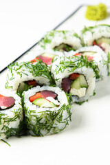 Sushi rolls with tuna, cucumber and cream-cheese in chopped dill. Served on a white plate over white background.