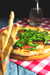 Rustic tasty pizza with meat, mushrooms, tomatoes and basil. Over wooden table, photo in dark tones.