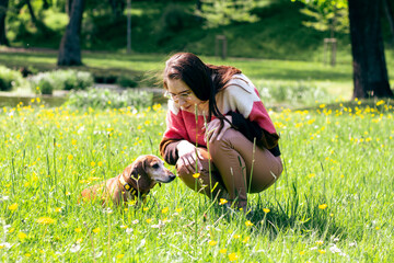Charming young lady dressed in coloful sweater playing with her daschund dog. Animal love concept