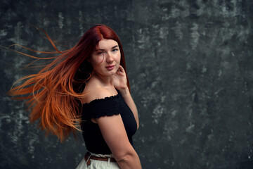 Naklejka premium high resolution portrait of a redhead caucasian girl with long hair fluttering in the wind posing on a gray background