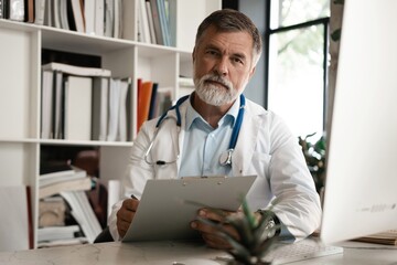 Portrait of handsome doctor sitting at desk, taking notes or fills in the client's medical card or prescribes medication