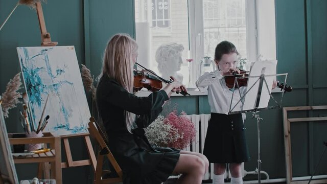 A girl playing violin during lesson with blonde woman teacher plays violin too